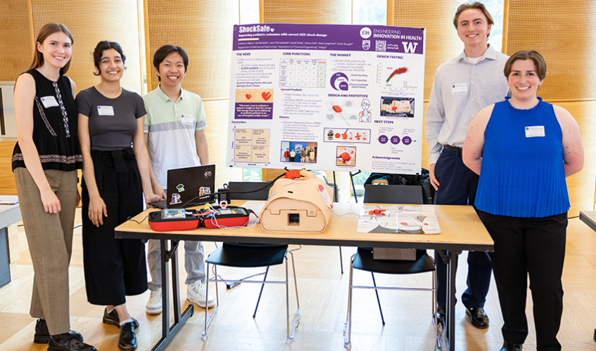 Five ShockSafe team members stand next to their poster and their prototype of their device.