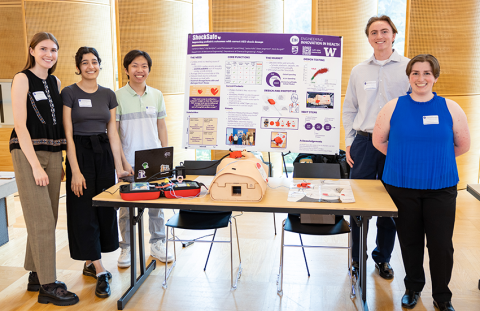 Five ShockSafe team members stand next to their poster and their prototype of their device.